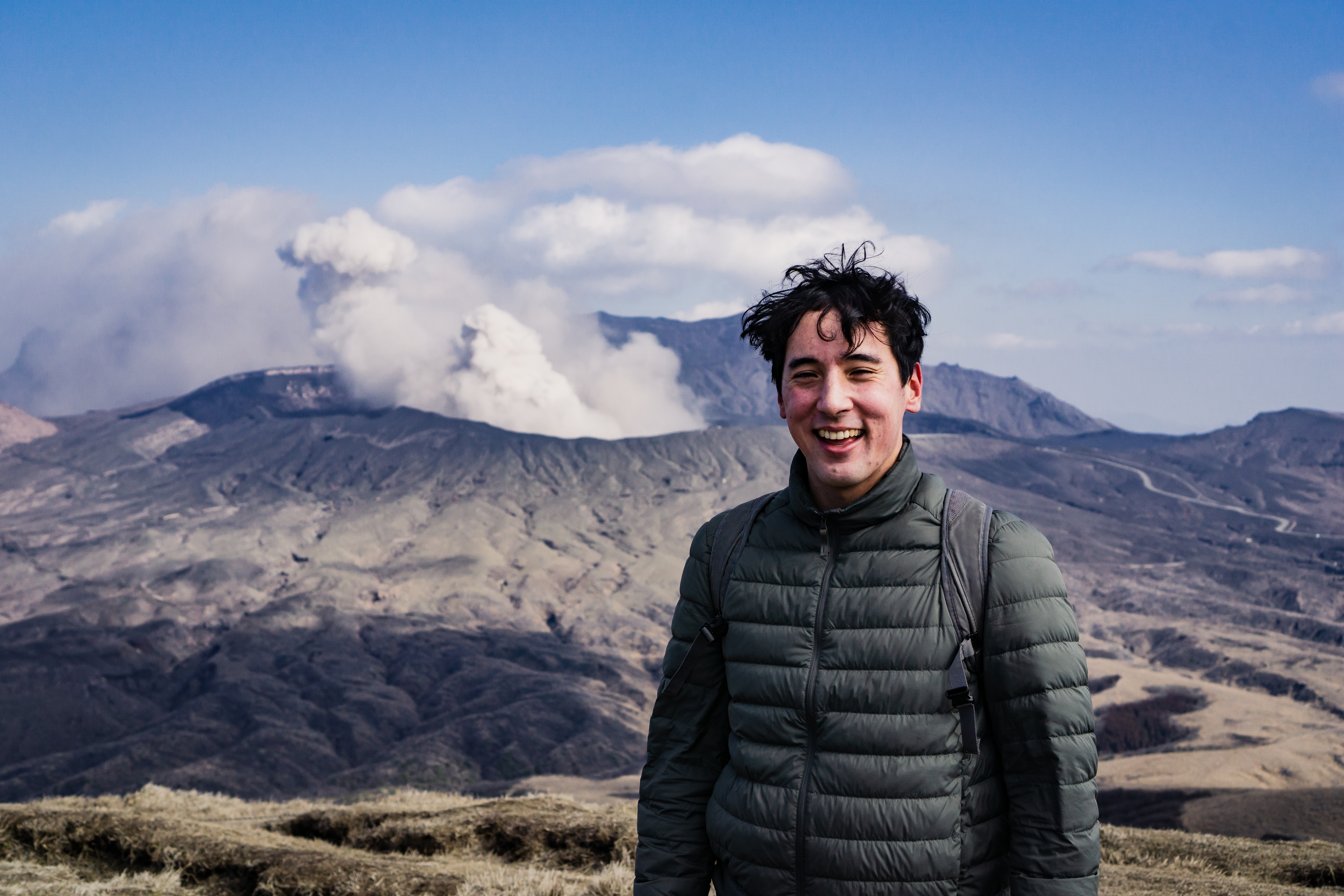 A man poses for a photo with Aso Volcano in the backdrop.